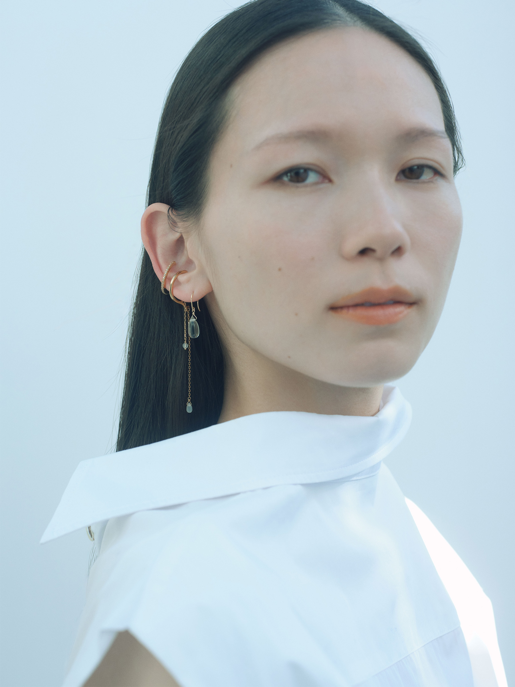 グリーンクォーツのドロップピアスとゴールドコーティングのイヤーカフを着用したモデル