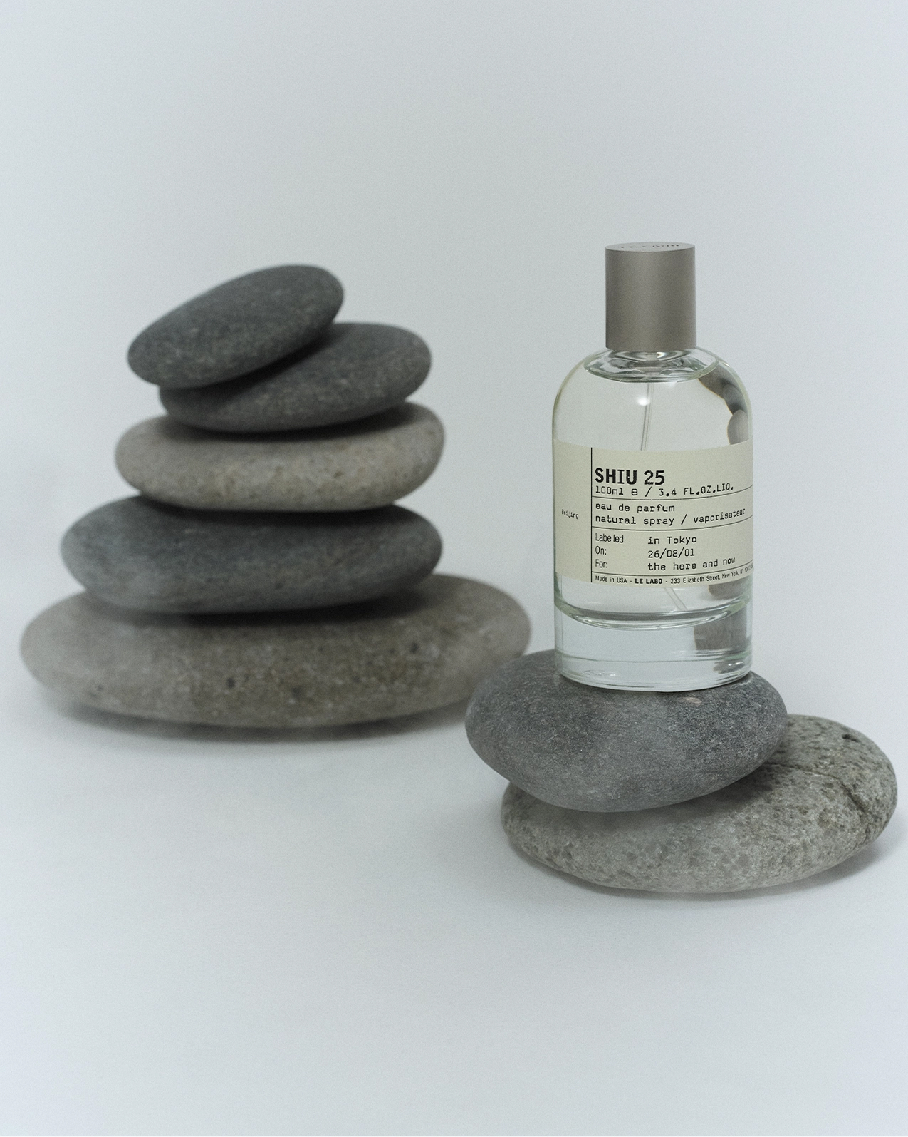 写真: Le Labo SHIU 25の香水ボトルが積まれた石の上に置かれている